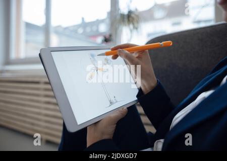 Hand einer Geschäftsfrau, die im Büro Windturbine auf einem Tablet-PC zeichnet Stockfoto