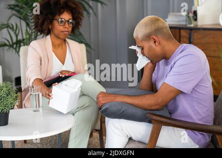 Gestresster Patient, der Tränen mit Gesichtsgewebe abwischt, sitzt vom Psychologen am Arbeitsplatz Stockfoto