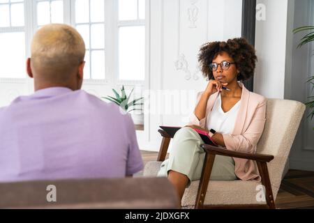 Psychologe, der im Sessel sitzt und den Patienten im Büro ansieht Stockfoto