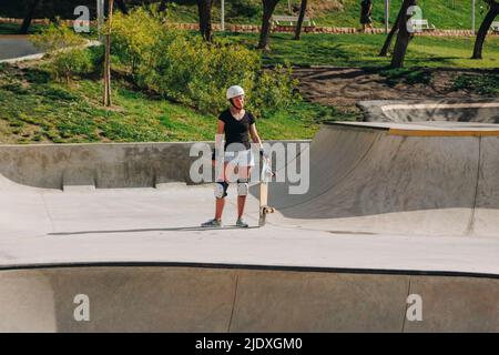 Frau trägt schützende Sportkleidung und hält Skateboard auf der Rampe Stockfoto