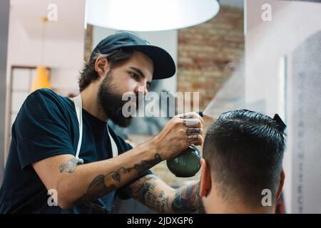 Friseur sprüht Wasser auf die Haare des Kunden im Friseurladen Stockfoto