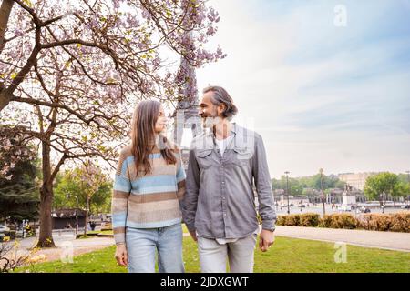 Lächelndes reifes Paar, das sich beim Spaziergang vor dem Eiffelturm, Paris, Frankreich, ansieht Stockfoto