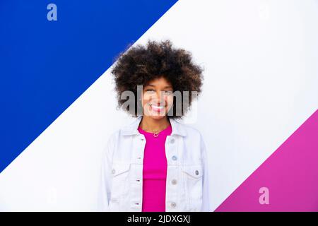 Fröhliche, junge Afro-Frau vor einer bunten Wand Stockfoto