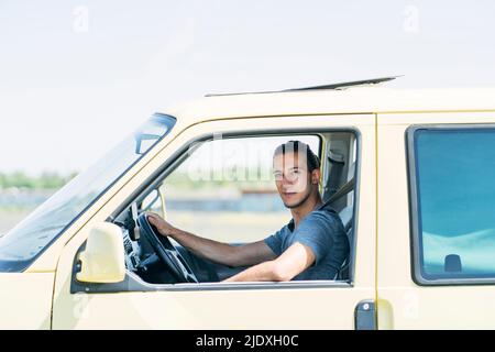 Hübscher junger Mann, der an einem sonnigen Tag in einem Lieferwagen sitzt Stockfoto