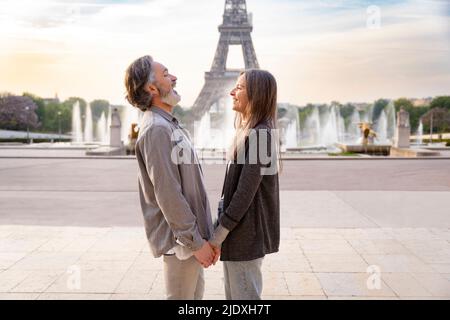 Glückliches reifes Paar, das die Hände vor dem Eiffelturm, Paris, Frankreich, hält Stockfoto