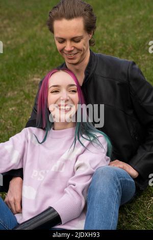 Lächelndes junges Paar, das auf Gras sitzt Stockfoto