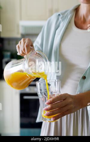 Hände einer Frau, die Orangensaft aus dem Krug in das Glas gießt Stockfoto