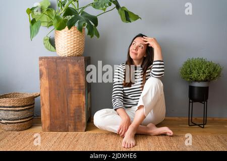 Kontemplative Frau mit Kopf in den Händen, die zu Hause auf dem Boden sitzt Stockfoto