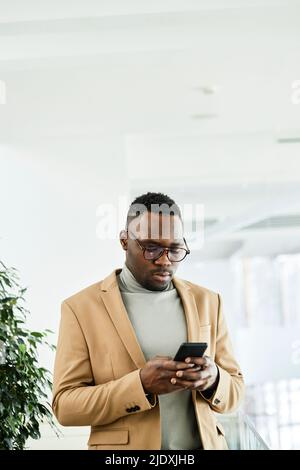 Junger Geschäftsmann mit Brille, der im Büro über das Mobiltelefon im Netz surft Stockfoto
