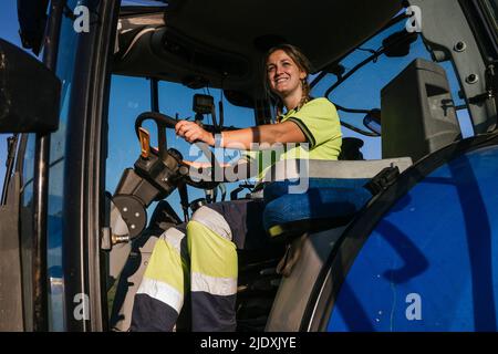 Lächelnde Bäuerin, die an einem sonnigen Tag im Traktor sitzt Stockfoto