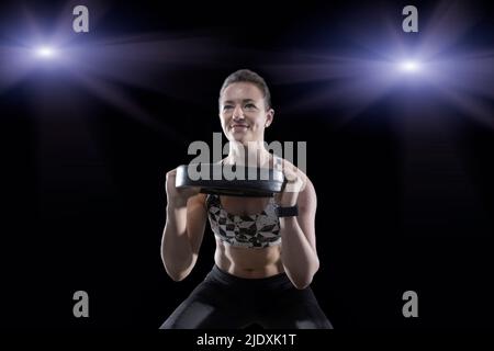 Lächelnde junge Frau, die die Hantelscheibe im Fitnessraum hebt Stockfoto