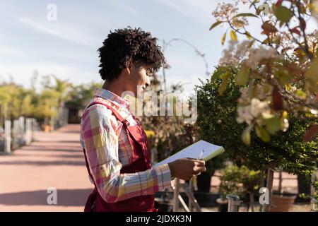 Junger Gärtner hält Buch in der Nähe von Pflanzen im Kindergarten stehen Stockfoto