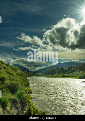 Ein Sturm auf dem Shoshone River in Cody Wyoming. Sehen Sie einen Sonnenaufbruch mit dunklen Wolken am Himmel. Der Fluss läuft rasant schnell, wenn man in Richtung Yellowstone schaut. Stockfoto