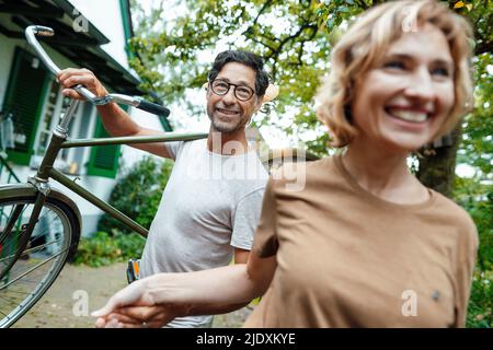 Reife Frau mit Mann, der Fahrrad auf der Schulter im Hinterhof trägt Stockfoto