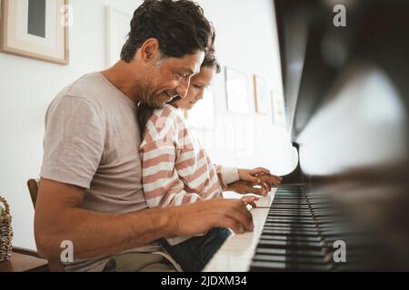 Glücklicher Vater, der zu Hause seiner Tochter Klavier beibringt Stockfoto