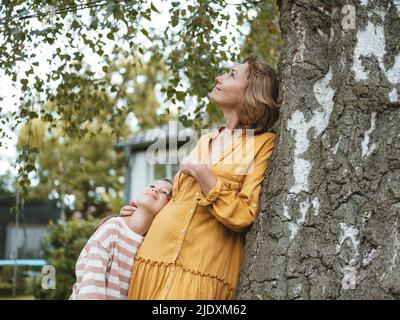 Lächelnde Mutter mit Tochter, die sich auf den Baumstamm lehnt Stockfoto