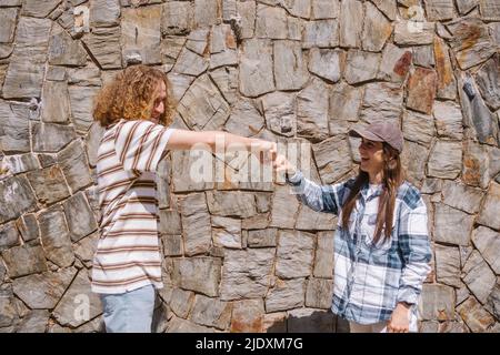 Lächelnder Mann, der seiner Freundin an einem sonnigen Tag vor der Wand eine Faust gab Stockfoto