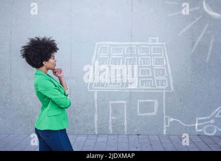 Junge Frau, die ein bemaltes Haus mit Sonnenkollektoren an der Wand ansieht Stockfoto