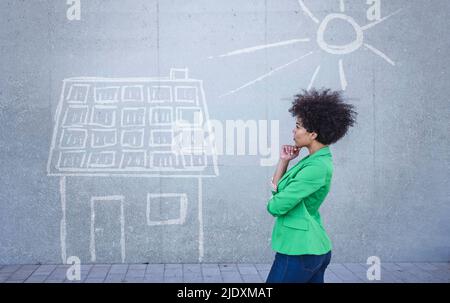 Junge Frau, die ein bemaltes Haus mit Sonnenkollektoren an der Wand ansieht Stockfoto