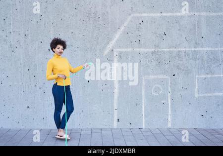 Junge Frau mit grünem Stecker, die vor einem bemalten Haus steht Stockfoto