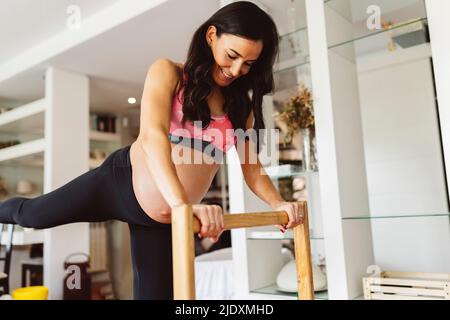 Lächelnde Schwangere mit Stand, der zu Hause Yoga macht Stockfoto