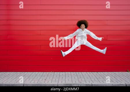 Fröhliche junge Frau macht Splits vor der roten Wand Stockfoto