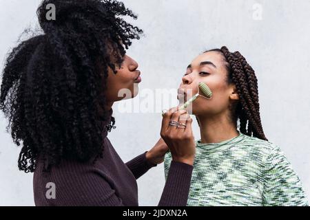 Frau, die einem Freund eine Massage mit Jaderolle vor weißem Hintergrund gibt Stockfoto