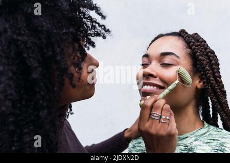 Lächelnde Frau mit Jadewalze auf Freund vor weißem Hintergrund Stockfoto