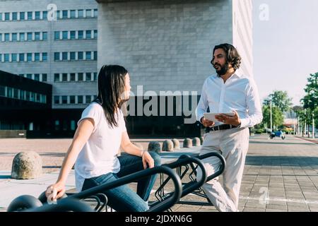 Geschäftsmann im Gespräch mit einem Kollegen, der in der Stadt auf einem Fahrradständer sitzt Stockfoto