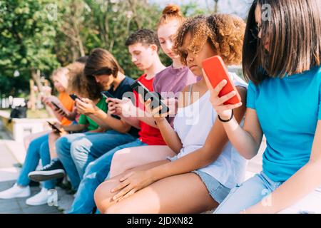 Multirassische Freunde, die an sonnigen Tagen Mobiltelefone nutzen Stockfoto