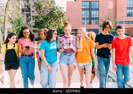 Lächelnde, multirassische Freunde, die Smartphone benutzen, um zusammen zu gehen Stockfoto