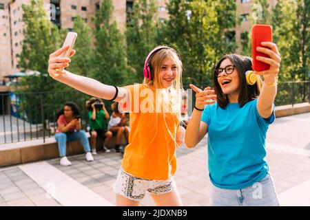 Freunde, die kabellose Kopfhörer tragen, genießen das Smartphone Stockfoto