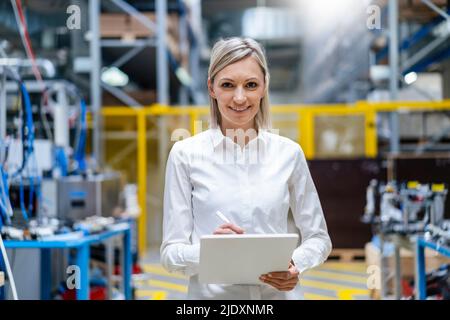 Porträt einer lächelnden Geschäftsfrau, die im Werk ein digitales Tablet hält Stockfoto