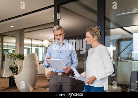 Geschäftsmann und Geschäftsfrau mit digitalem Tablet und Dokumenten im Büro Stockfoto