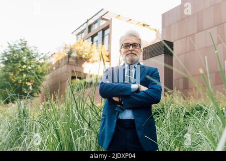 Ein Geschäftsmann, der mit gekreuzten Armen im Büropark steht Stockfoto