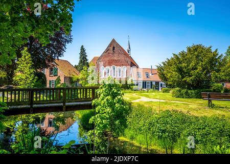 Deutschland, Niedersachsen, Krummhorn, kleine Brücke über stehendes Wasser mit Loquard-Kirche im Hintergrund Stockfoto