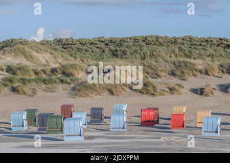 Deutschland, Niedersachsen, Juist, mit Kapuze bedeckte Strandliegen vor grasbewachsenen Dünen Stockfoto