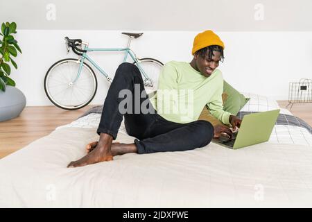 Lächelnder Geschäftsmann, der im Schlafzimmer an einem Laptop arbeitet Stockfoto