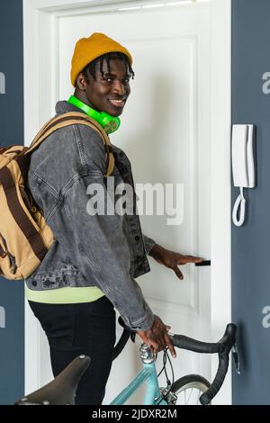 Junger Mann, der die Tür mit dem Fahrrad zu Hause öffnet Stockfoto