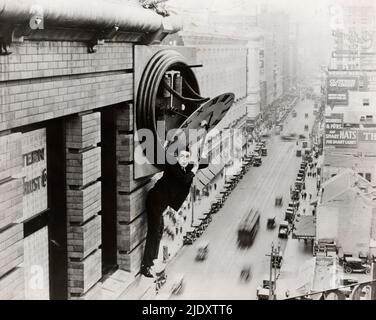 Harold Lloyd in einer ikonischen Szene aus Safety Last, in der Lloyd am Ende an einem großen Uhrgebäude hoch über einer belebten Straße hängt. Stockfoto