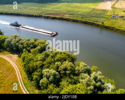 Kleines Schleppboot schiebt Barge entlang ruhigem Wasser vorbei an Feldern Stockfoto