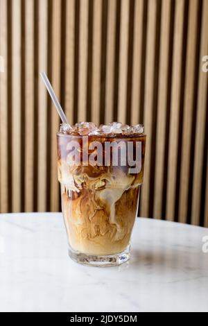 Schönes kaltes Gebräu mit Creme, die auf einem weißen Marmortisch wirbelt Stockfoto