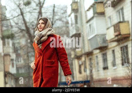 Schöne Brünette in einem roten Mantel auf einer Stadtstraße unter dem Schnee. Stockfoto