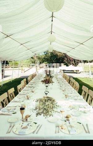 Langer Tisch mit Kerzen, Blumen und Tischläufer. Hochzeitstisch Stockfoto