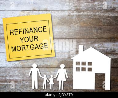 Text mit Refinanzierung Ihrer Hypothek Schreiben Sie auf einem gelben Haftnotiz und Home Family Paperon Holztisch Hintergrund. Hypothekenkonzept. Stockfoto