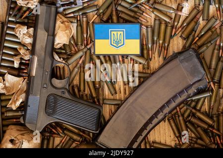 Pistolenkartuschen und eine Zeitschrift mit Patronen und einem Streifen auf der Kleidung eines Soldaten die Flagge der Ukraine sind in einer Kiste, Munitions und Waffen Stockfoto