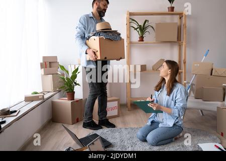 Junges Paar verpackt und überprüft Sachen mit Checkliste vor dem Umzug in ein neues Haus oder eine neue Wohnung Stockfoto