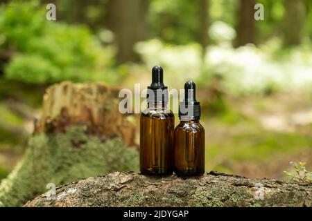 Zwei glasbraune Kosmetikbehälter mit Pipette werden vor dem Hintergrund eines natürlichen Waldes platziert. Konzept der natürlichen Bio-Kosmetik, Hautgesundheit. S Stockfoto