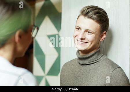 Frau, die mit einem hübschen jungen Mann im Rollkragen sprach, während sie in der modernen Lobby stand Stockfoto