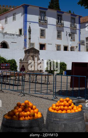 Zeit für eine Erfrischung an einem heißen Sommermorgen ... reife, saftige Orangen, die bereit sind, in kühlende Getränke gepresst zu werden, ausgestellt in Praça de Santa Maria, dem gepflasterten Hauptplatz der mittelalterlichen Stadtmauer von Óbidos, Centro, Portugal. Stockfoto